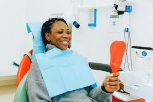 Smiling woman holding a mirror during a dental check-up in a clinic.